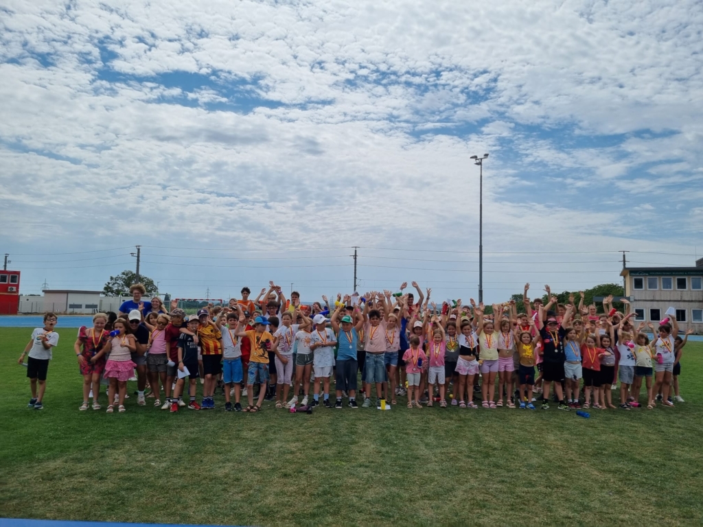 Kinder mit Medaillen und erhobenen Armen stehen auf einem Sportplatz in Österreich.