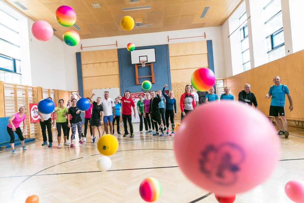 Gruppe wirft im Turnsaal bunte Bälle