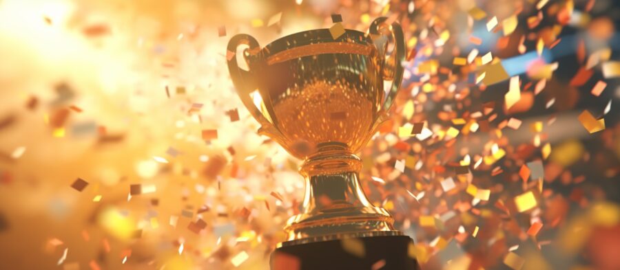 Golden trophy cup with confetti on golden background.