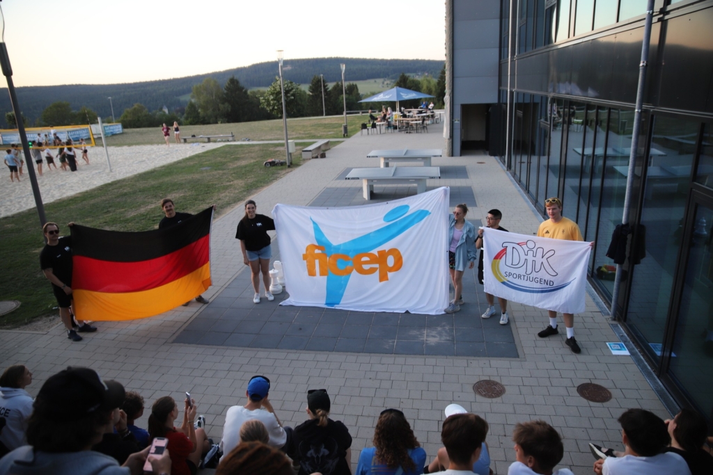 Jugendliche halten Fahnen, darunter die deutsche Flagge, vor einem Gebäude.