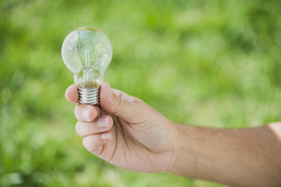 human-hand-holding-transparent-light-bulb-against-green-backdrop